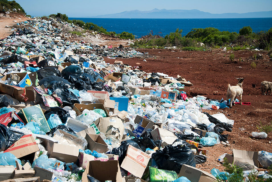 Terreno con basura acumulada a la orilla del mar, y montañas al fondo