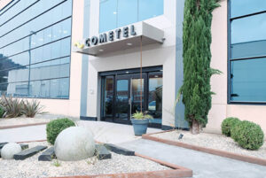 Acceso principal a oficinas de Cometel Recycling con ventanas y puertas de cristal, con arbustos y arboles afuera
