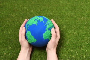 Manos sosteniendo esfera que simula ser un planeta Tierra, sobre pasto verde, haciendo referencia al Día Internacional contra el Cambio Climático