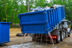 Camión de carga azul, derramando lixiviados en suelo junto a árboles, producto del mal tratamiento de residuos