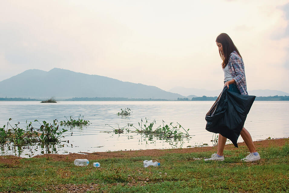 Mujer recogiendo basura en pradera junto a lago, ejemplificando el concepto de Mottainai